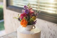 25 a wedding cake topped with a vintage teacup and lots of colorful blooms to make it bolder