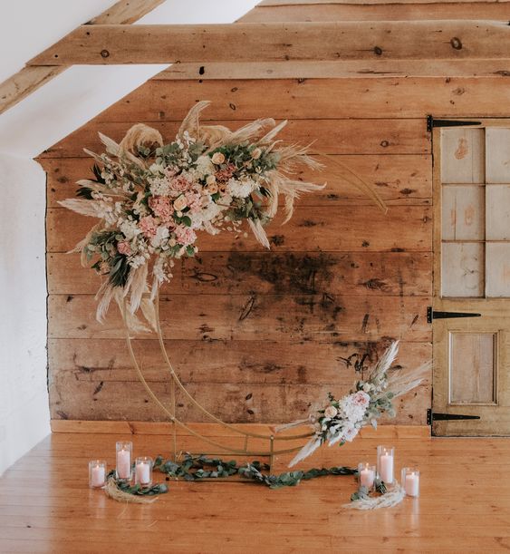 a boho celestial wedding altar of a metal half moon, white and blush blooms, greenery and pampas grass and pillar candles