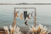 a boho celestial wedding arch with half moons, a dream catcher, white blooms and pampas grass for a celestial wedding