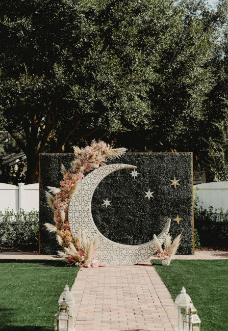 a boho wedding altar with a carved half moon and pampas grass plus stars in the backdrop is a cool solution
