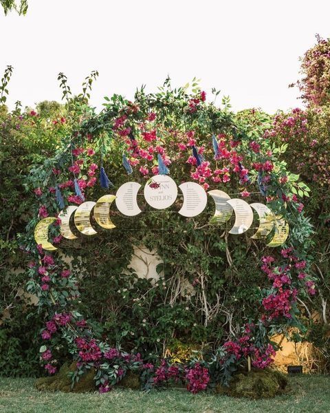 a boho wedding seating chart placed on a round wedding arch with blooms and greenery, with a chart placed on phases of the moon pendants
