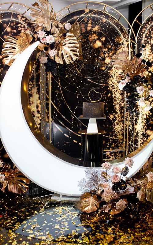 a bold and glam celestial wedding backdrop with a half moon, gold monstera leaves and foil, blush blooms and gold leaves