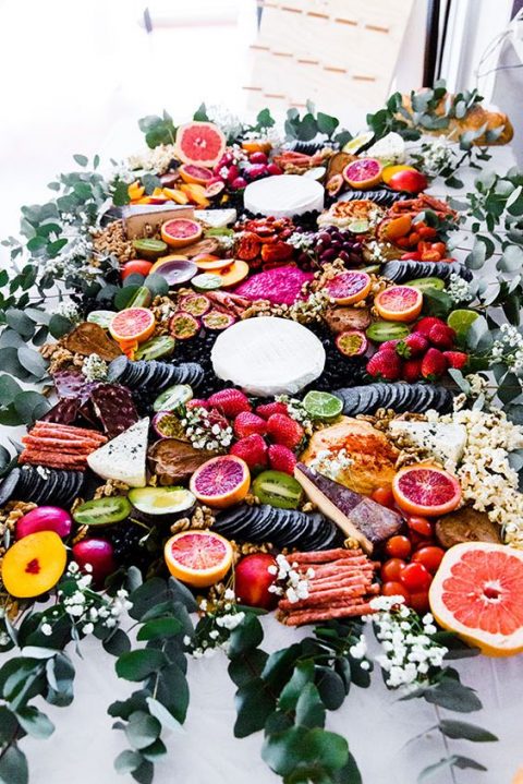 a bright grazing table with cheese, fruits and berries and crackers pls baby’s breath and greenery for decor