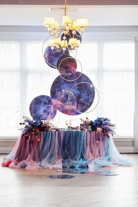 a bright wedding tablescape with a pink, teal and blue tulle tablecloth, celestial spheres and bold blooms on the table