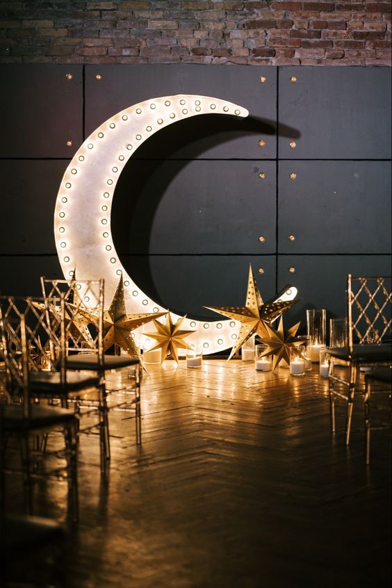 a catchy celestial wedding backdrop with a marquee half moon, candles, stars and elegant chairs is a cool and bold idea