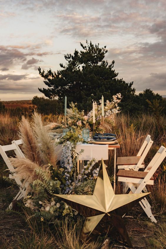 a celestial outdoor wedding tablescape with pastel blooms, pampas grass, dark porcelain and a large gold star