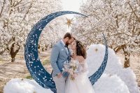 a celestial wedding altar with a blue half moon with constellations, faux clouds and stars right in a blooming orchard