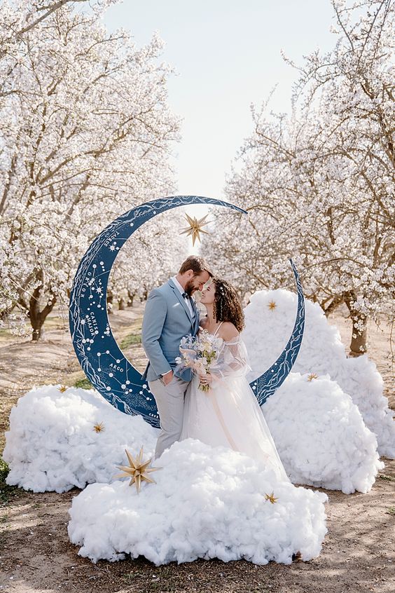 a celestial wedding altar with a blue half moon with constellations, faux clouds and stars right in a blooming orchard