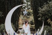 a celestial wedding altar with a half moon piece, some purple and blue blooms and greenery and copper star candleholders