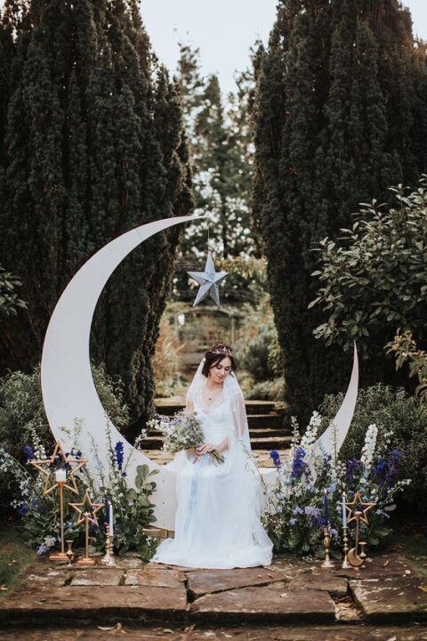 a celestial wedding altar with a half moon piece, some purple and blue blooms and greenery and copper star candleholders