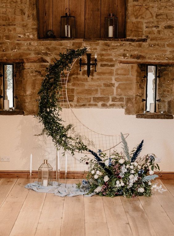 a celestial wedding backdrop of a half moon, neutral blooms and greenery, pampas grass, candles and candle lanterns