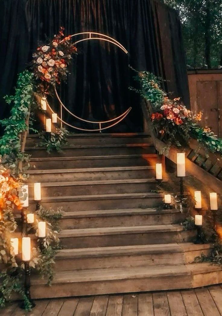 a celestial wedding backdrop with a half moon decorated with blooms, with a stais done with greenery, blooms and candles