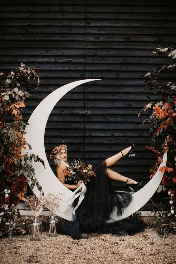 a celestial wedding backdrop with a half moon, greenery and blooms plus dried grasses for a celestial wedding
