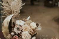 a celestial wedding centerpiece of a half moon, white and neutral blooms and grasses, rocks and a candle