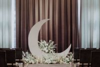 a celestial wedding ceremony space with a half moon and white blooms and candles, matching arrangements along the aisle