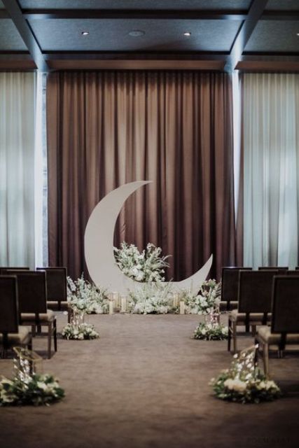 a celestial wedding ceremony space with a half moon and white blooms and candles, matching arrangements along the aisle