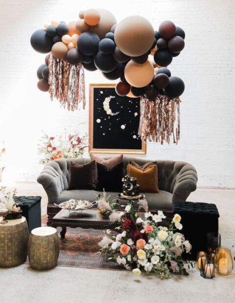 a celestial wedding lounger with a grey sofa, side tables and a black pouf, balloons, an artwork and some blooms