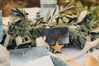 a celestial wedding tablescape with gold placemats, grey porcelain and grey watercolor stationery, gold stars and greenery