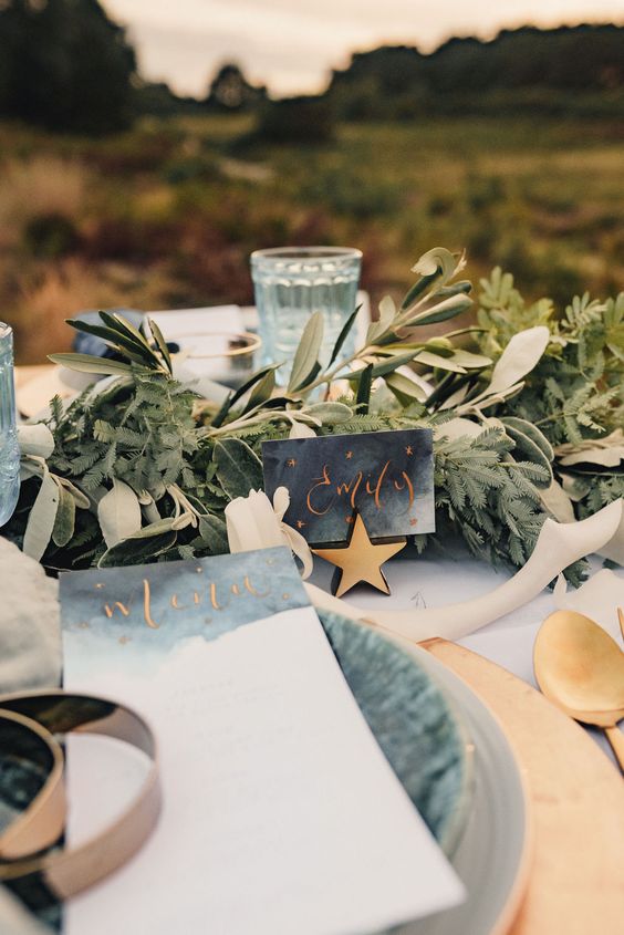 a celestial wedding tablescape with gold placemats, grey porcelain and grey watercolor stationery, gold stars and greenery