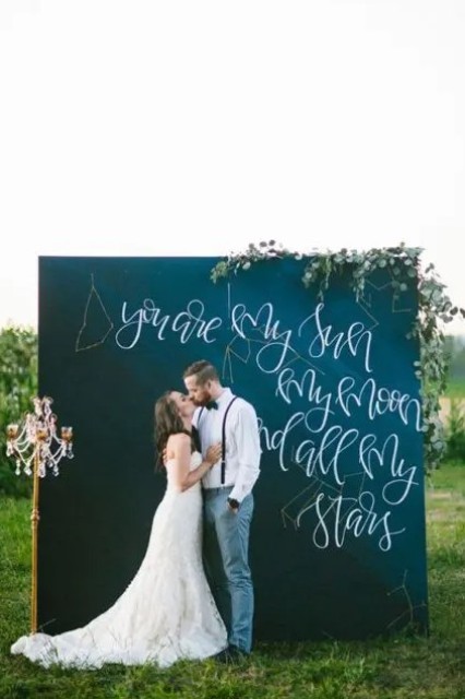 a chalkboard wedding backdrop with greenery and blooms and a quote dedicated to the galaxies and stars