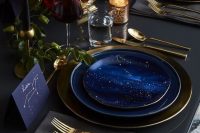 a dark and refined wedding tablescape with blue starry plates, matching cards, gold cutlery, dark blooms and candles for an astronomy wedding
