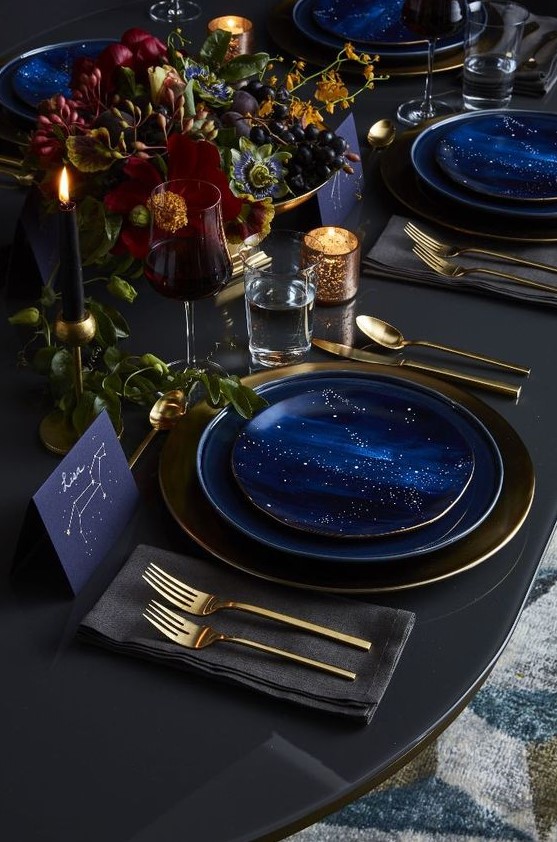 a dark and refined wedding tablescape with blue starry plates, matching cards, gold cutlery, dark blooms and candles for an astronomy wedding