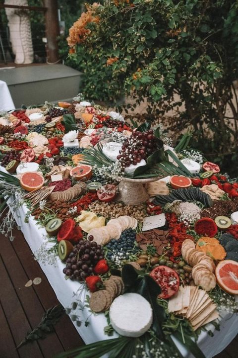 a gorgeous grazing table with fruits and berries and various kind sof cheese and crackers plus some blooms for decor