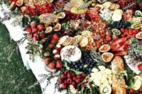 a grazing table with lots of berries and fruit, bread and cheese, herbs and even wildflowers for decor