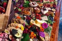 a lush and colorful grazing table with crackers, fruits and berries, nuts and dried fruit, dips and bright blooms