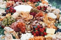a lush grazing table with charcuterie, cheese, berries and fruits, olives and nuts