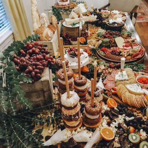 a luxurious multi layer grazing table with charcuterie, cheese, fruits, berries, bread in a box and glazed donuts on stands
