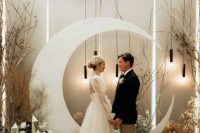 a modern celestial wedding backdrop of a half moon, white blooms, mirror pieces, pendant lamps and branches