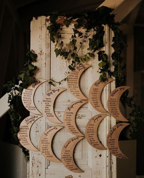 a moon shaped seating chart decorated with greenery is a cool idea for a celestial wedding