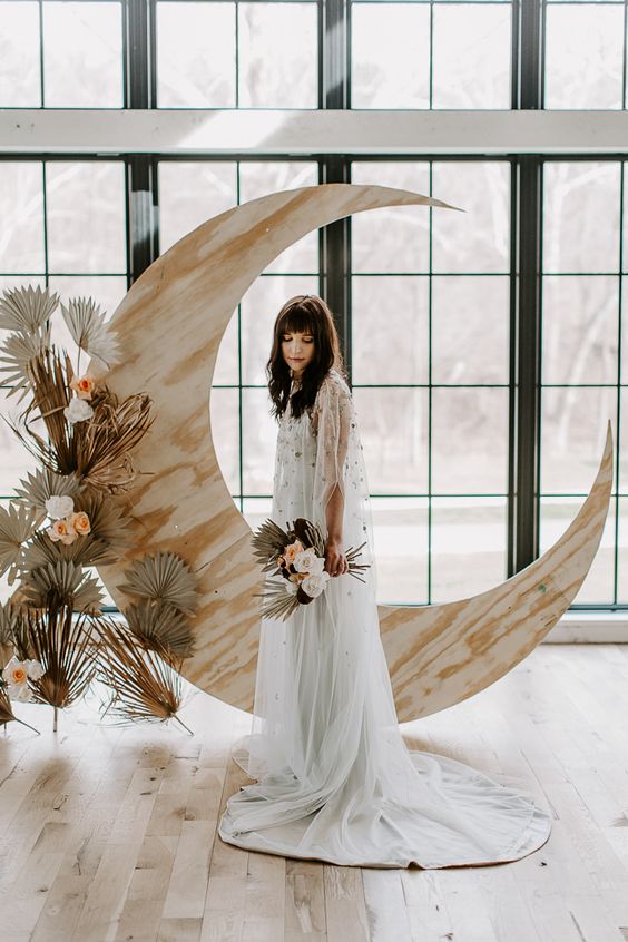 a neutral celestial wedding altar of a plywood half moon and some fronds and blooms is a stylish and chic idea