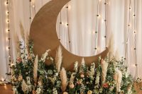 a pretty celestial wedding altar with a half moon and a lush floral arrangement with pampas grass is a cool idea