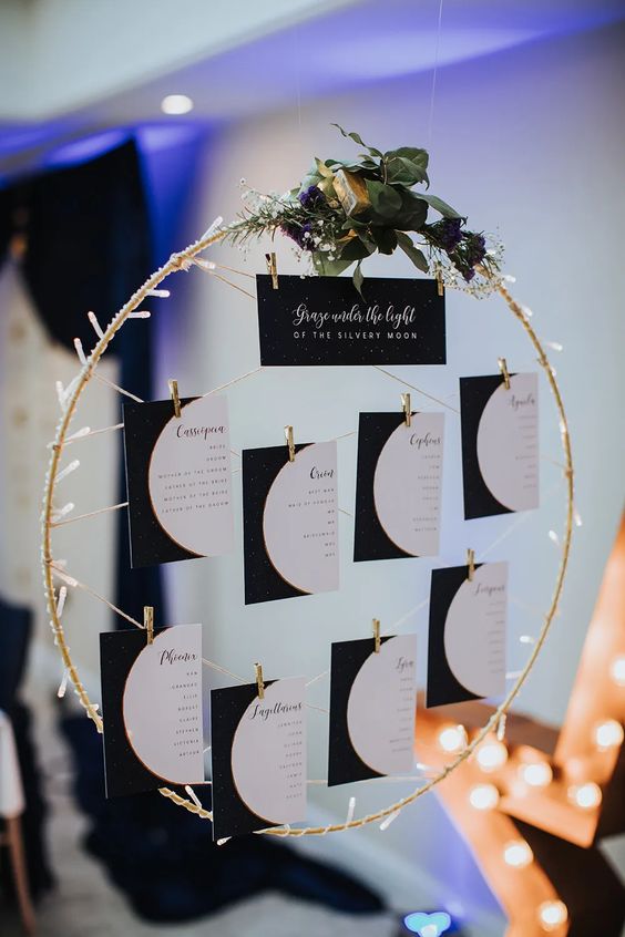 a pretty celestial wedding seating chart with an embroidery hoop and moon phases, lights and greenery on top
