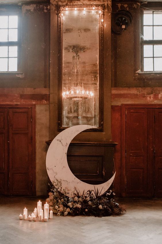 a stylish and moody celestial wedding altar with a half moon, dark florals and pillar candles is an elegant idea