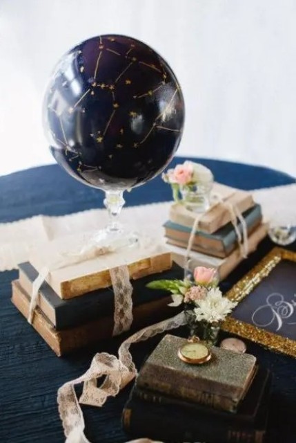 an astronomy wedding centerpiece of vintage books, blooms, a watch and a navy and gold sky globe