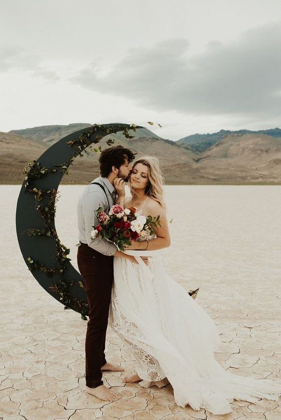 an unusual black half moon wedding altar decorated with foliage and placed in the desert