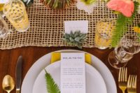a colorful wedding tablescape with ferns, billy balls, a yellow mesh table runner, succulents, gold touches and blooms