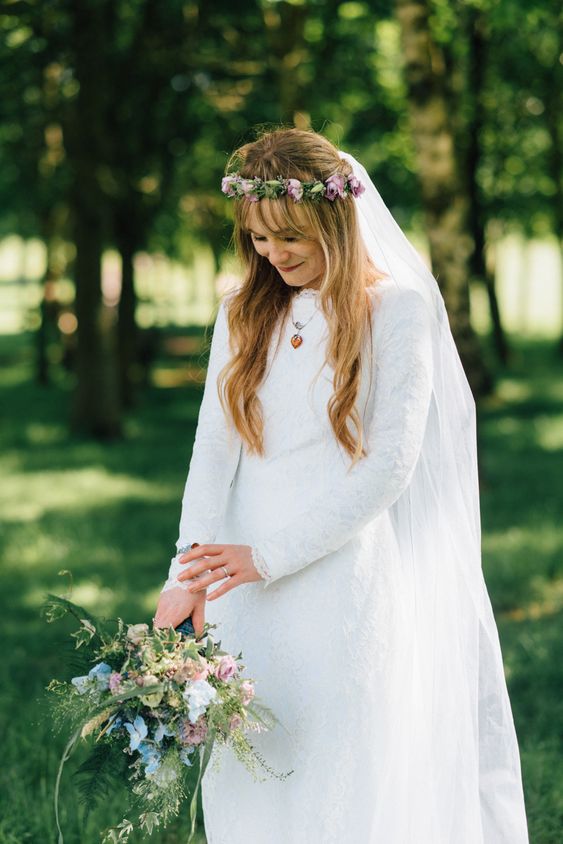a lace sheath wedding dress with a high neckline and long sleeves paired with a floral crown for a 70s inspired bridal look