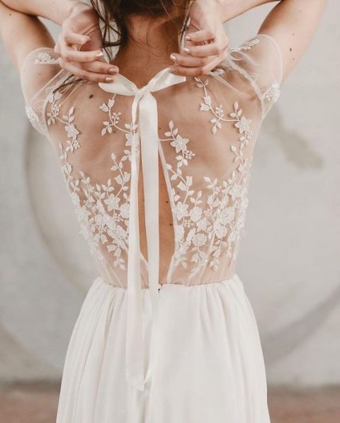 a romantic wedding gown with illusion lace back with a slight cutout and a bow and a flowy plain skirt