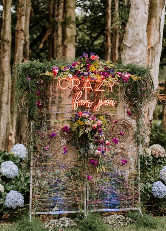 The wedding backdrop was done with colorful yarn and blooms, with a neon sign and greenery on top