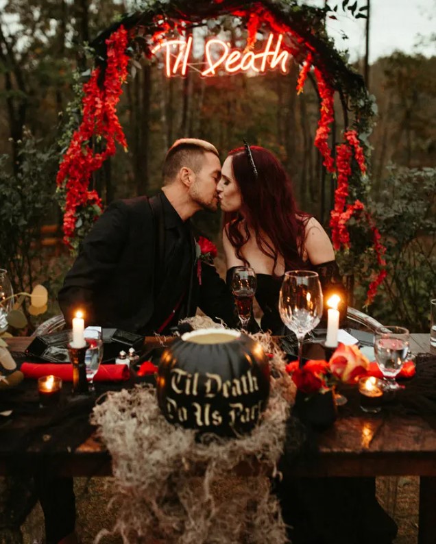 a Halloween wedding arch decorated with greenery, red blooms and a red neon sign is a bold modern idea to rock