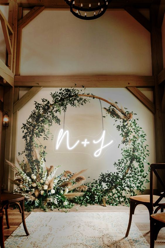 a boho round wedding arch decorated with greenery, with pampas grass and white blooms and neon monograms
