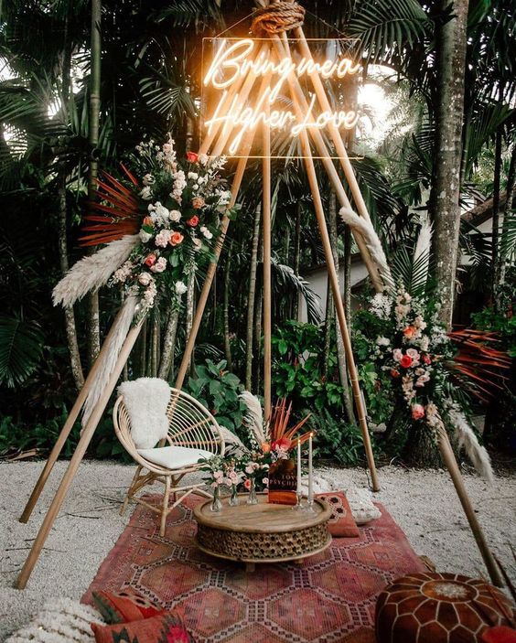 a boho wedding altar of neutral and pink blooms, greenery pampas grass, a neon sign on top is a cool idea