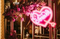 a bold wedding backdrop of a gilded frame, pink and fuchsia blooms and greenery, a pink neon heart is wow