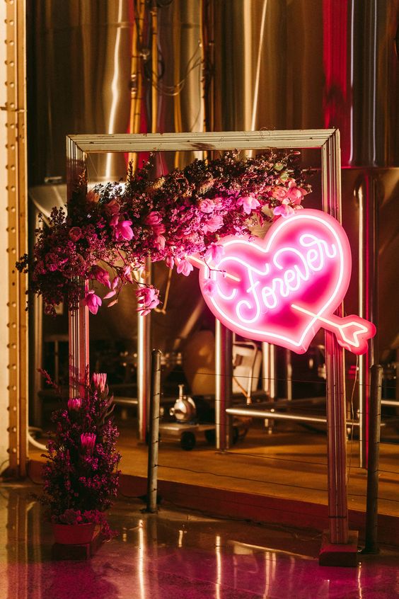 a bold wedding backdrop of a gilded frame, pink and fuchsia blooms and greenery, a pink neon heart is wow