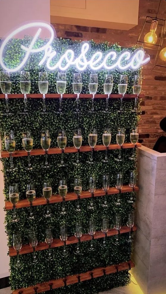 a boxwood wall with shelves-holders and a neon sign is a lovely modern idea to serve drinks at your wedding