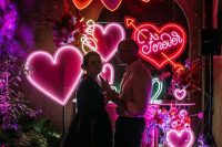 a bright neon heart wedding backdrop with a garland, colorful hearts and some blooms is amazing for a dance floor